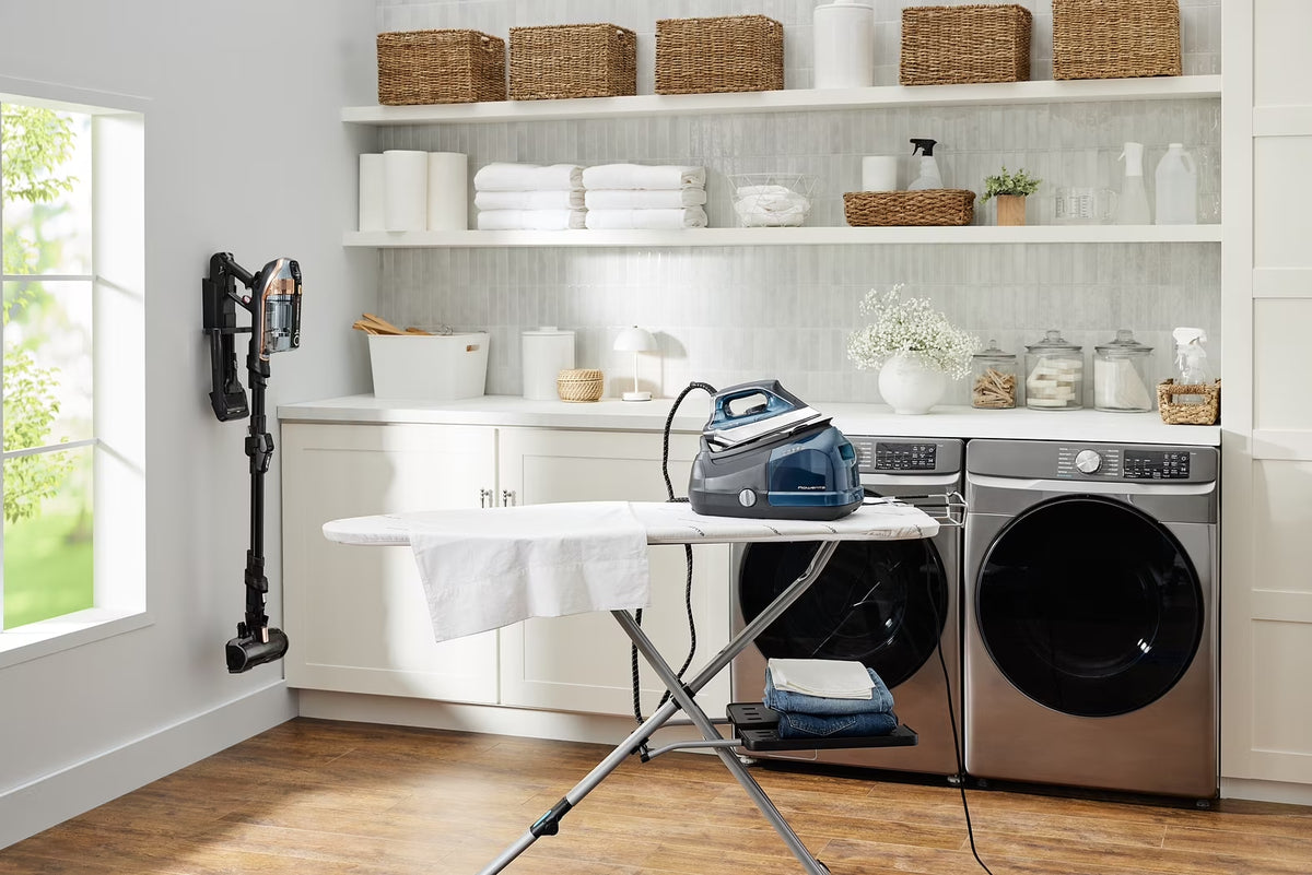 professional garment steamer on an ironing board in a modern laundry room with shelves.