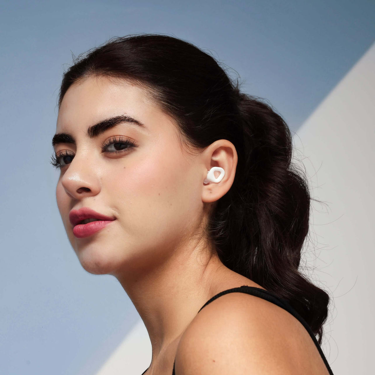 Model wearing ZENZ Unwind Pro noise reducing earplugs for better sleep in glacier white.