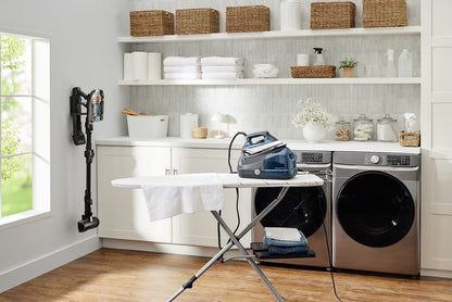 professional garment steamer on an ironing board in a modern laundry room with shelves.